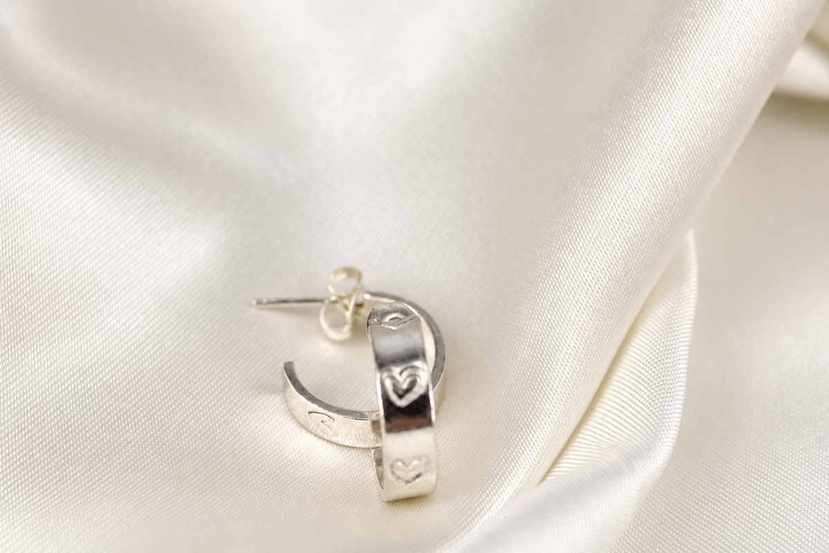 Pair of 15 mm sterling-silver Beloved Micro Hoops with hand-stamped hearts on cream satin.