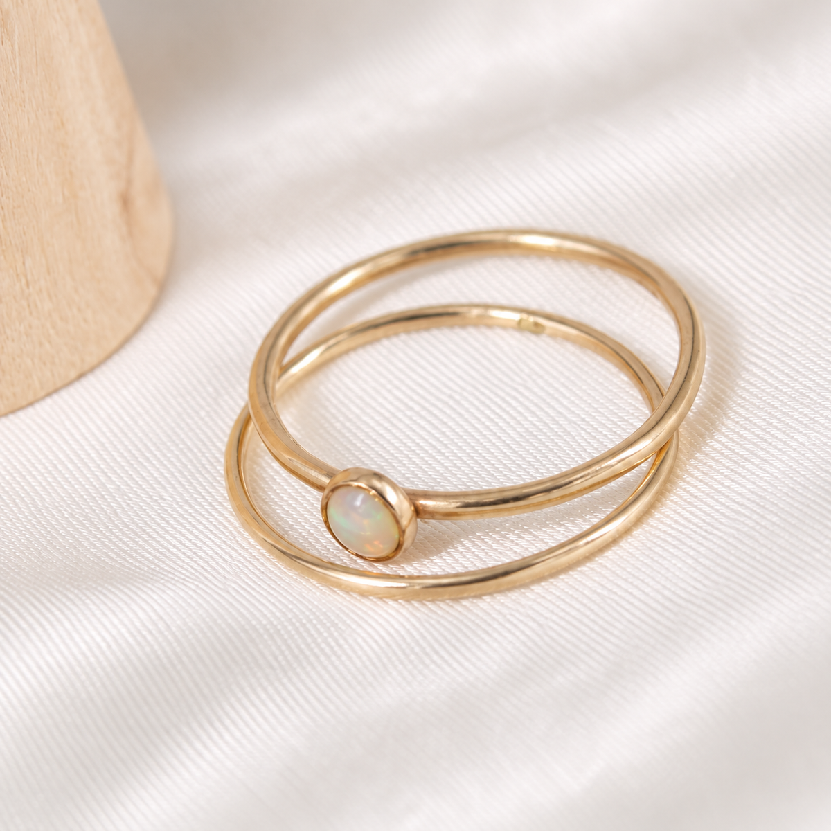 Two delicate 14k gold-filled rings, including a 4mm opal ring, arranged on ivory satin.