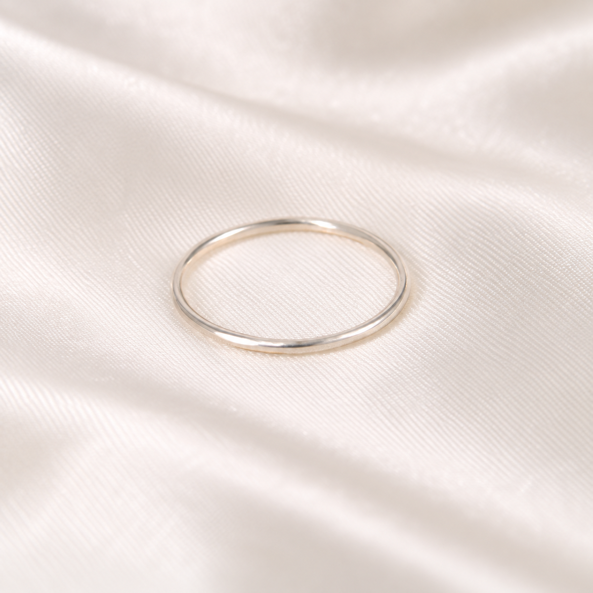 Simple 18-gauge sterling silver ring arranged on ivory satin.