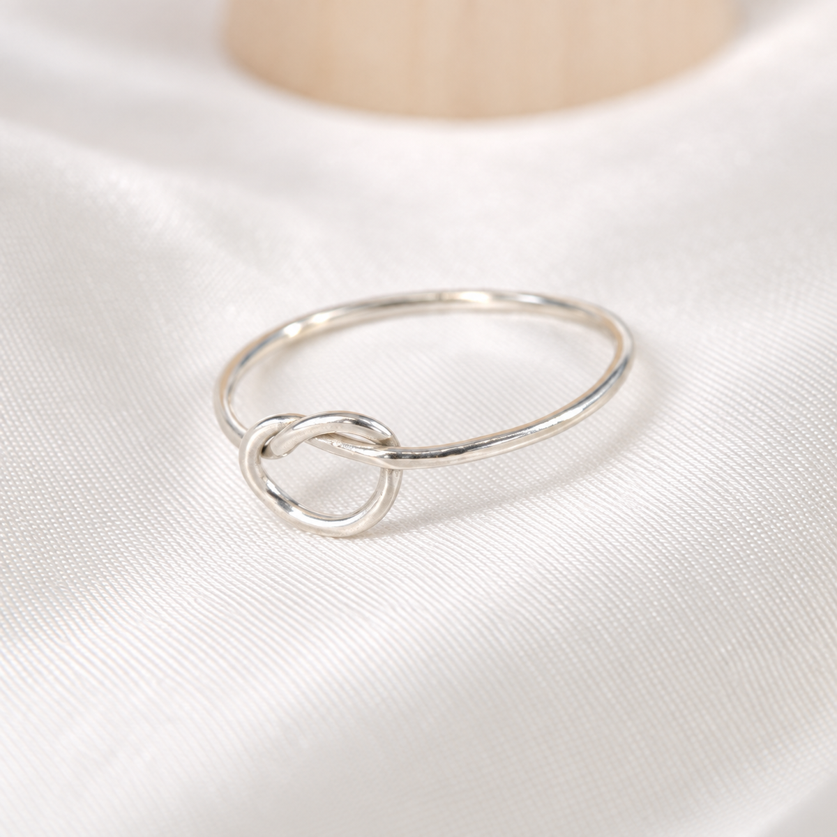 Dainty sterling silver knot ring arranged on ivory satin.