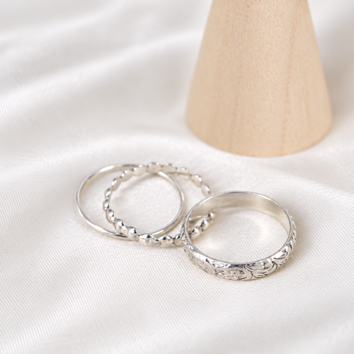 Three handmade sterling silver stacking rings arranged on ivory satin.