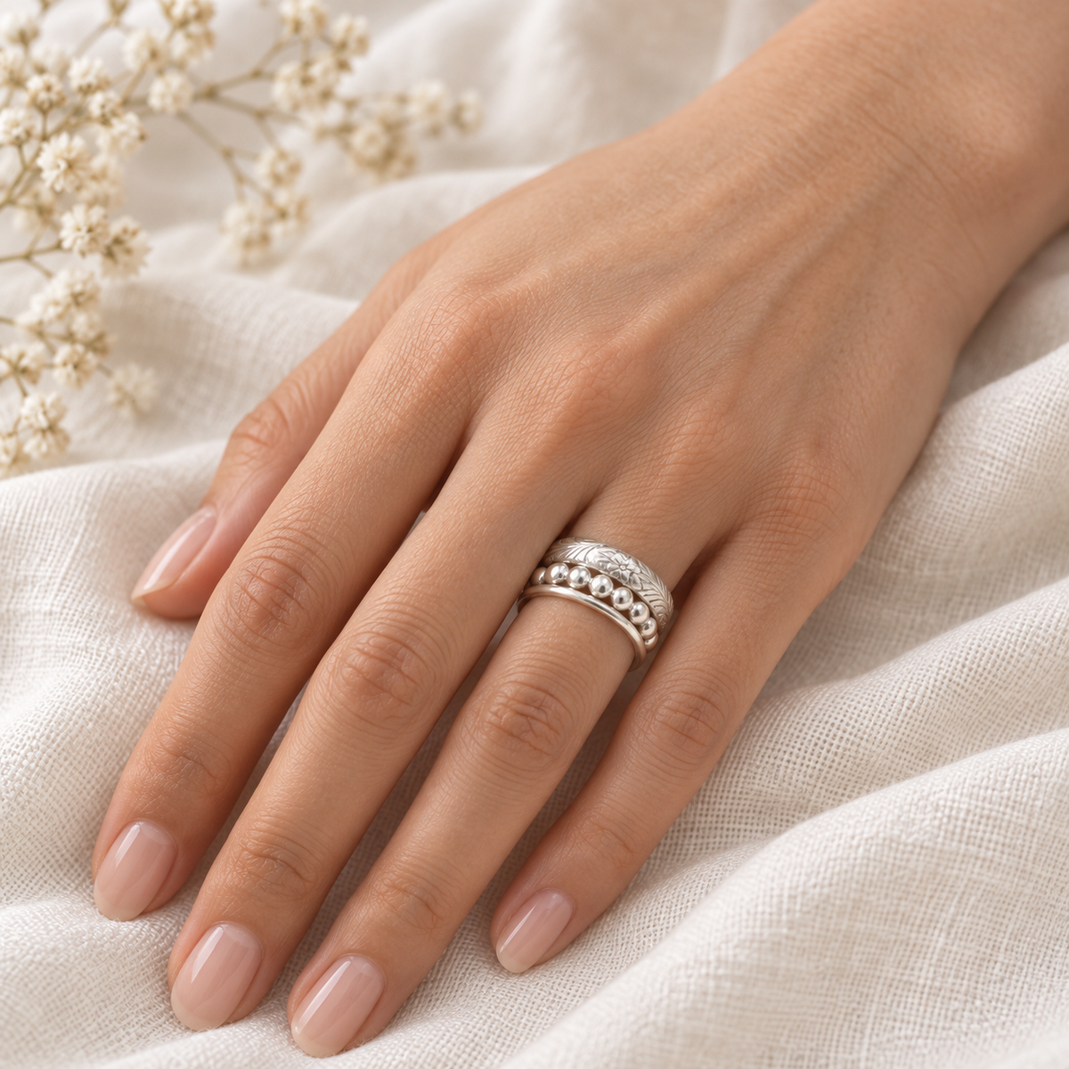 Sterling silver floral, beaded, and smooth stacking rings worn on a model’s hand.