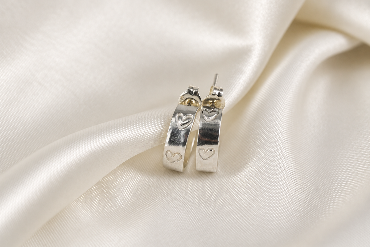 Close-up of a 15 mm sterling-silver Beloved Micro Hoop showing the hand-stamped heart details on cream satin.