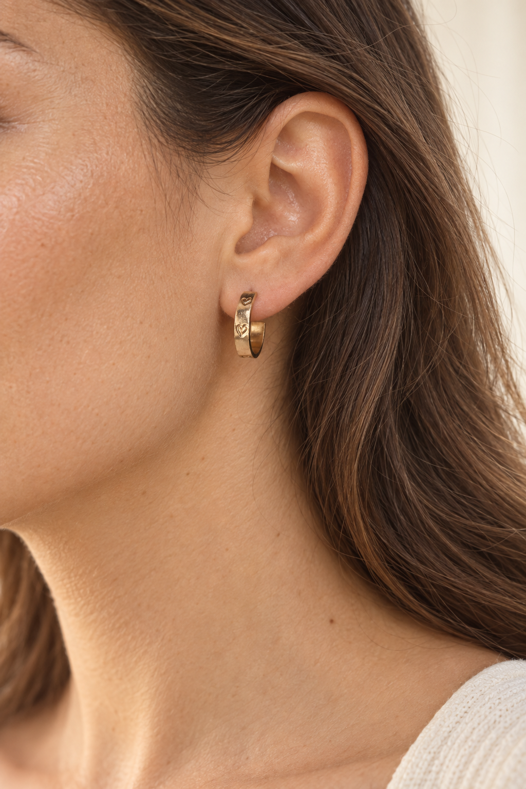 Side profile of a model wearing a 15 mm gold-filled Beloved Micro Hoop with hand-stamped hearts.