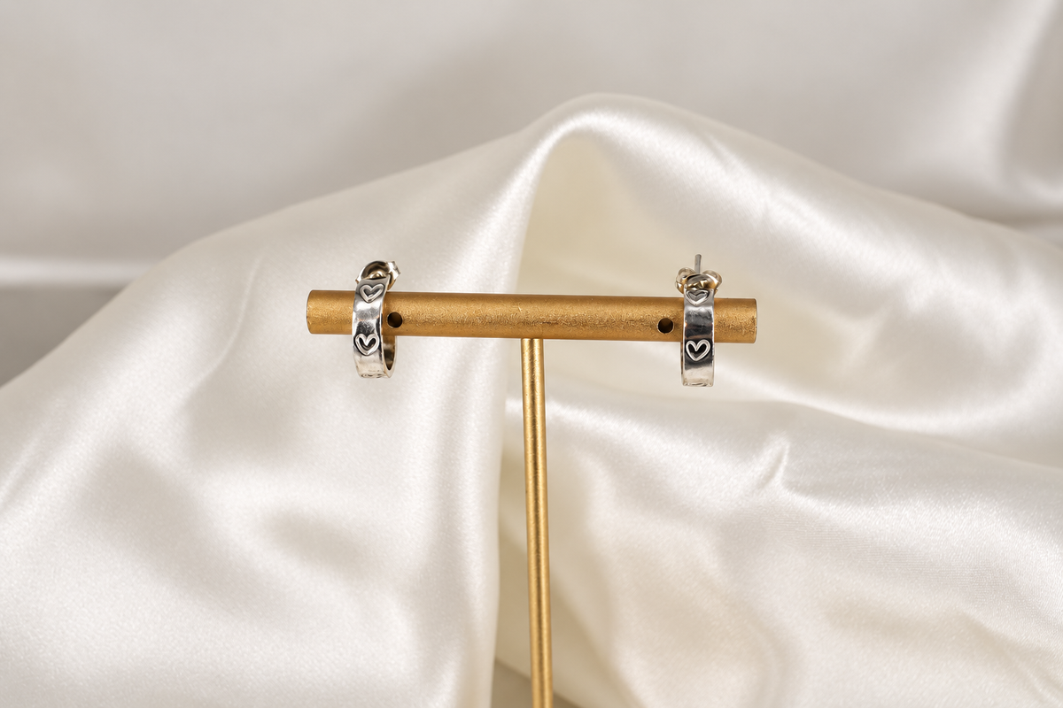 Pair of 15 mm sterling-silver Beloved Micro Hoops with hand-stamped hearts displayed on a gold earring stand.