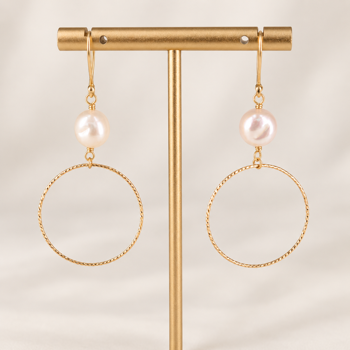 Isolde gold-filled freshwater pearl hoop earrings displayed on a gold jewelry stand