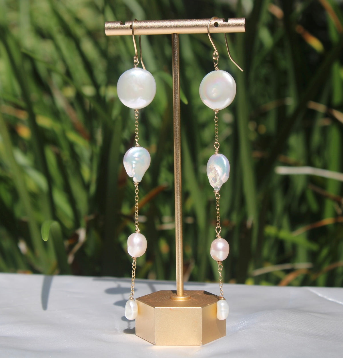 Cascading freshwater pearl shoulder-duster earrings with 14k gold-filled chain displayed on a gold stand