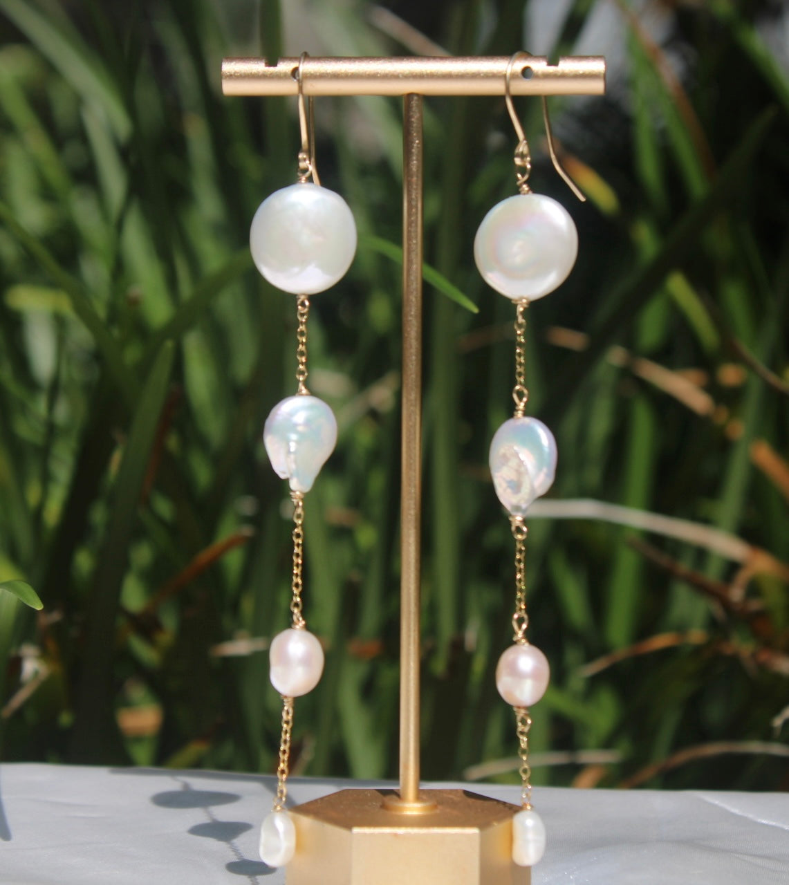 Close-up of long 14k gold-filled earrings with four differently shaped freshwater pearls on each earring.