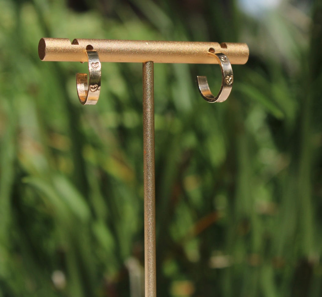 Handmade gold-filled micro hoop earrings with hand-stamped hearts displayed on a gold jewelry stand.