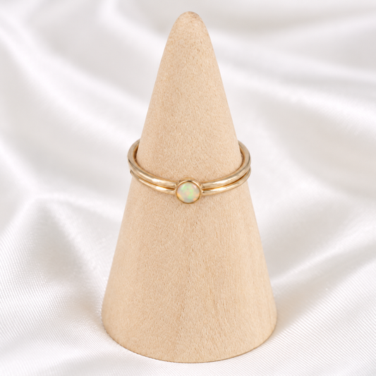Dainty 14k gold-filled opal ring stack displayed on a natural wooden cone.