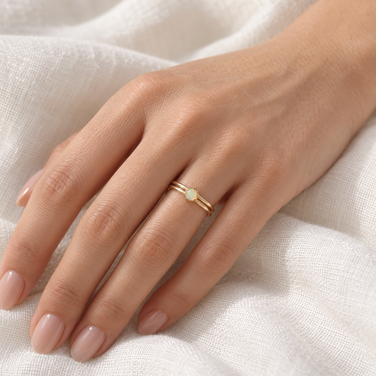 Dainty 14k gold-filled opal ring stack worn on a model’s hand.