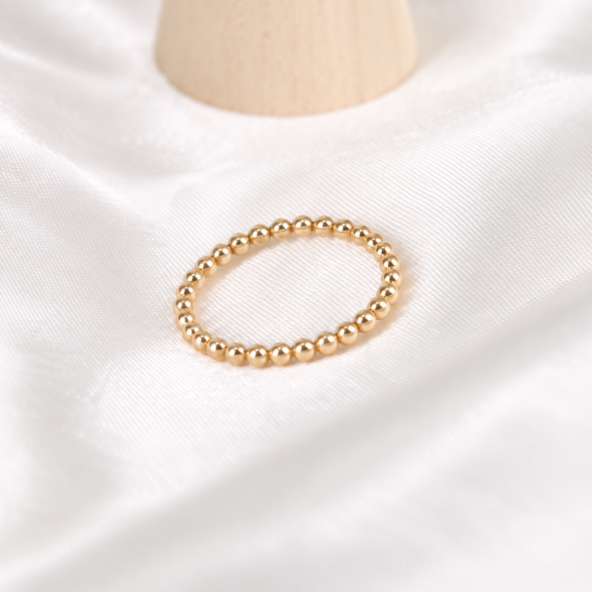 Dainty 14k gold-filled beaded stacking ring arranged on ivory satin.
