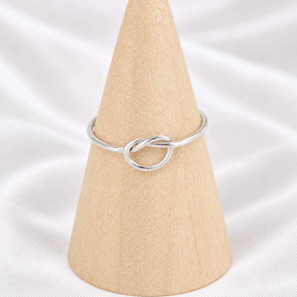 Handmade 18-gauge sterling silver knot ring displayed on a natural wooden cone.