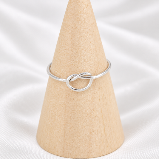 Handmade 18-gauge sterling silver knot ring displayed on a natural wooden cone.
