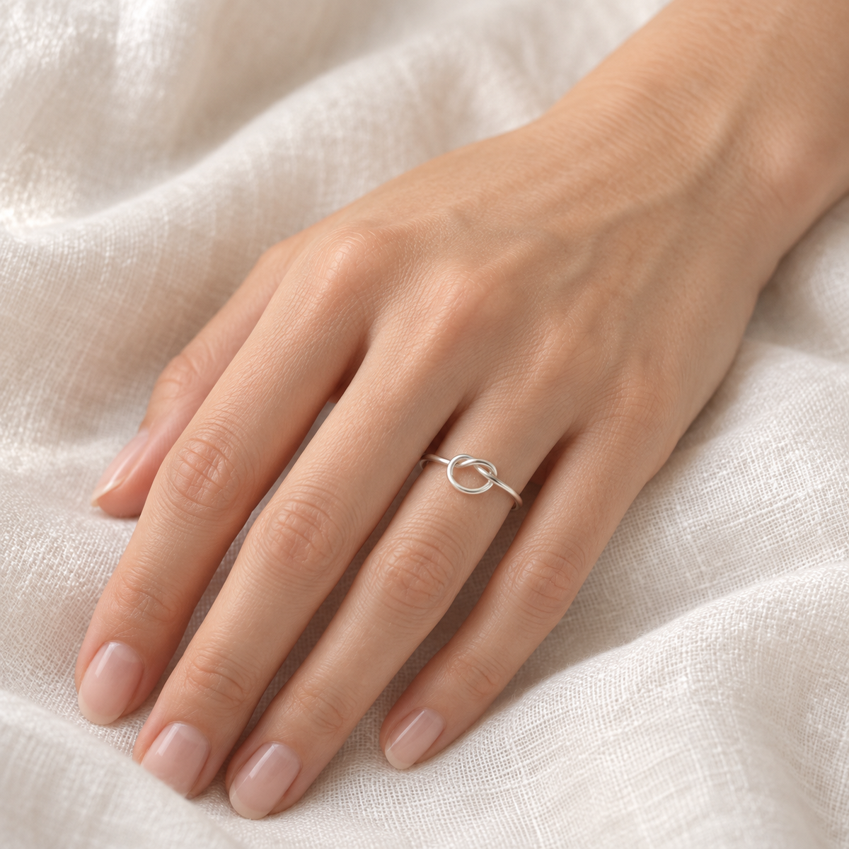 Dainty sterling silver knot ring worn on a model’s hand.