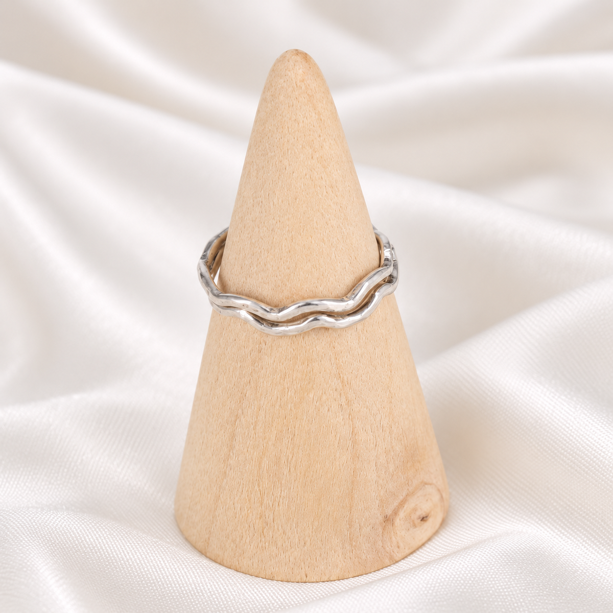 Two handmade sterling silver wavy stacker rings displayed on a natural wooden cone.