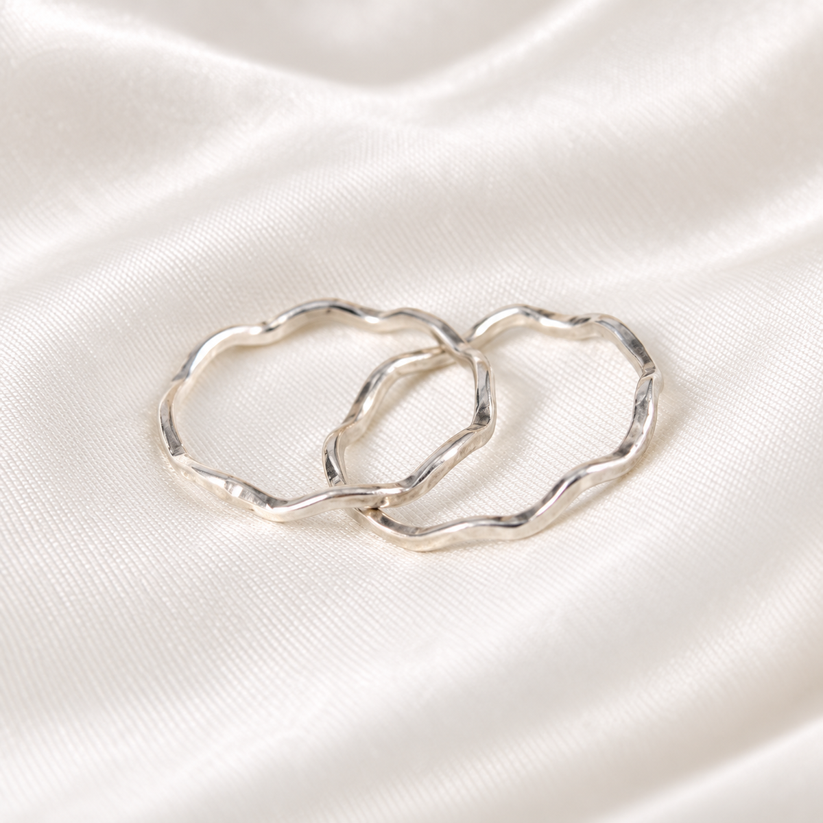 Three handmade sterling silver wavy rings arranged on ivory satin.