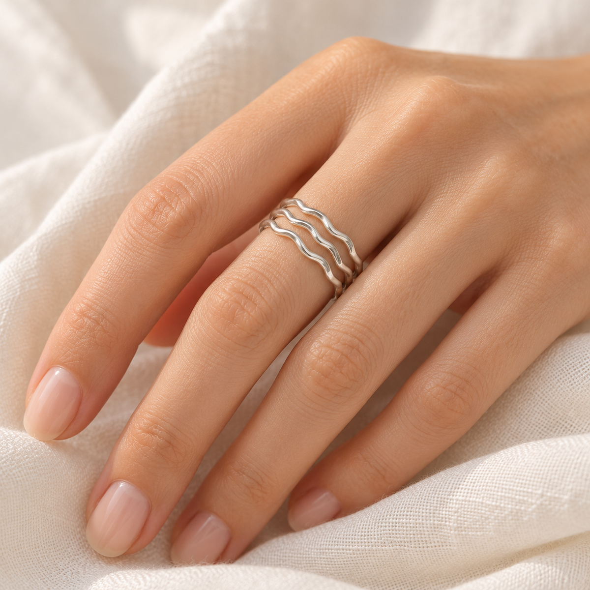 Three delicate sterling silver wavy stacker rings worn together on a model’s hand.
