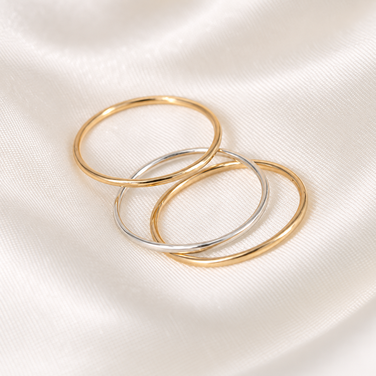 Three delicate gold-filled and sterling silver stacking rings arranged on ivory satin.